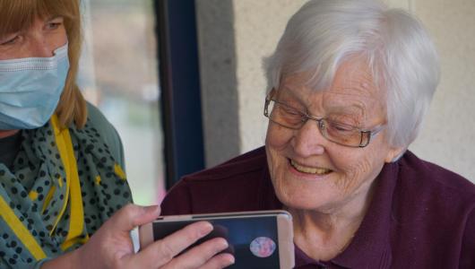 Vårdare visar en mobilskärm till en äldre kvinna