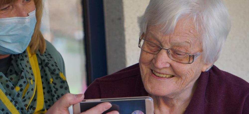 Vårdare visar en mobilskärm till en äldre kvinna